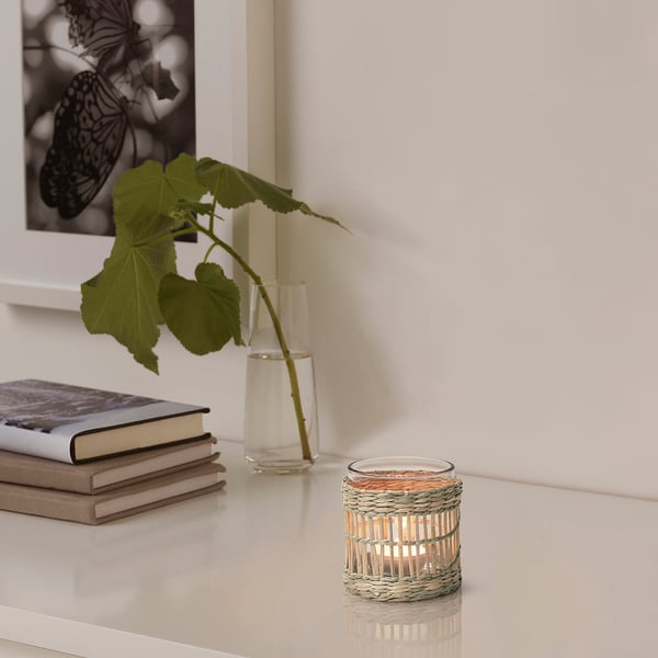 Tealight holder on table, handwoven from sedge, with plant and books.