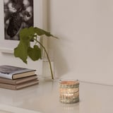 Tealight holder on table, handwoven from sedge, with plant and books.