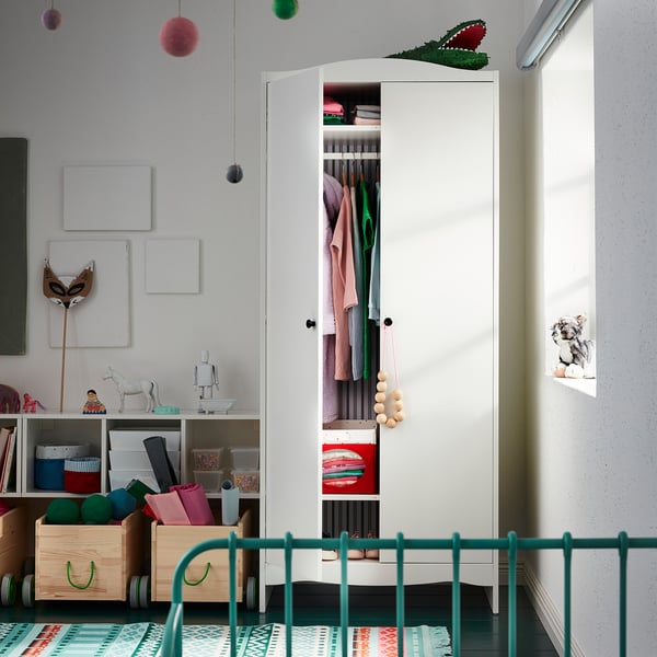 Childrens room with open white SMÅGÖRA storage unit, displaying clothes and toys. Green railing bed in foreground.