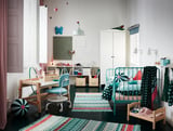 Bright childrens room with SMÅGÖRA turquoise shelf, wooden desk, blue chair & colorful rug.