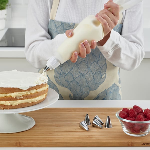 Baker decorates cake with whipped cream and berries.