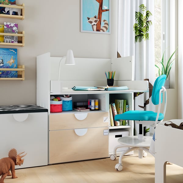 Childs room with white wooden desk, blue chair, shelves with books, dinosaur toy, lamp, and plant.