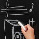 Hand writes music notes on blackboard; a creative and educational activity.
