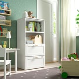Childrens room with white SMÅSTAD bookcase and shelves; bear toy, books, and crafts on shelves; green rug, white curtains, and wooden furniture.