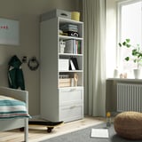 Gray and white SMÅSTAD bookcase with books, clothes, decor, a small bed, and framed art.