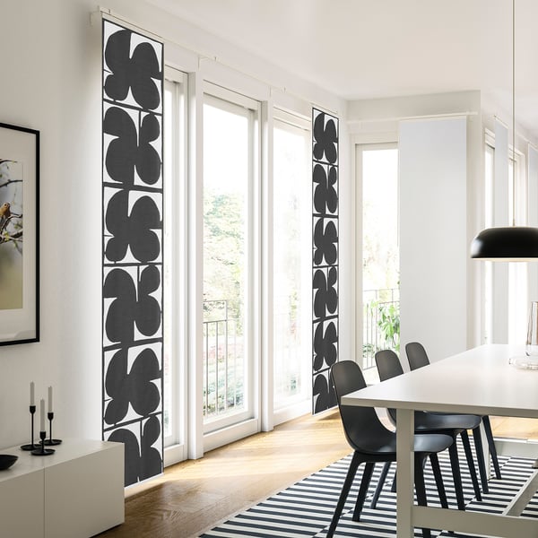 Modern living room with tall black-and-white curtains, dining table, black chairs, candlesticks, and striped rug, filled with natural light.