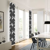 Modern living room with tall black-and-white curtains, dining table, black chairs, candlesticks, and striped rug, filled with natural light.