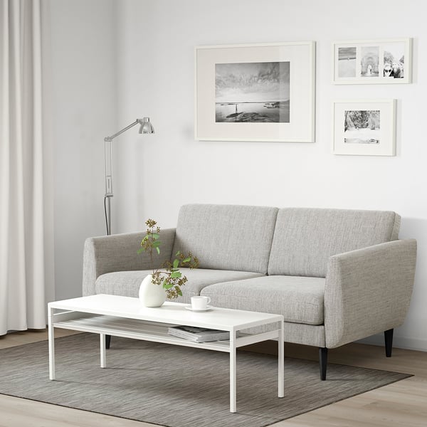 Sofa in minimalist living room with photos, flowers, lamp.