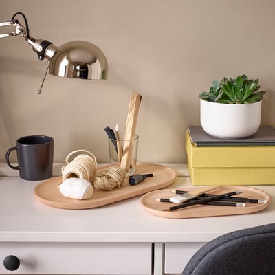 Desk with SMÖRLING trays, a mug, and a plant. Trays hold art supplies and rope. Bright and organized workspace with a lamp.