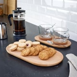 Assorted cookies on oval wooden trays, coffee cups, and french press on black countertop.