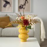 Bright yellow SMYCKA vase with mixed flowers on white table in cozy room.