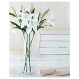 Vase with white lilies on table, white wall, marble countertop, rolled paper.