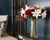 Vase with red and white artificial flowers on table, elegant room background.