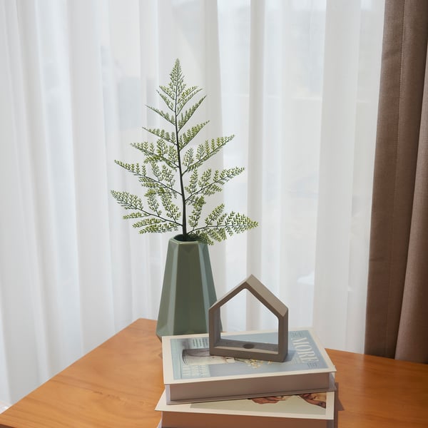 Green vase with plant on books near window.