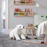 Large white stuffed polar bear sits beside bed, surrounded by toy train and books on shelves.