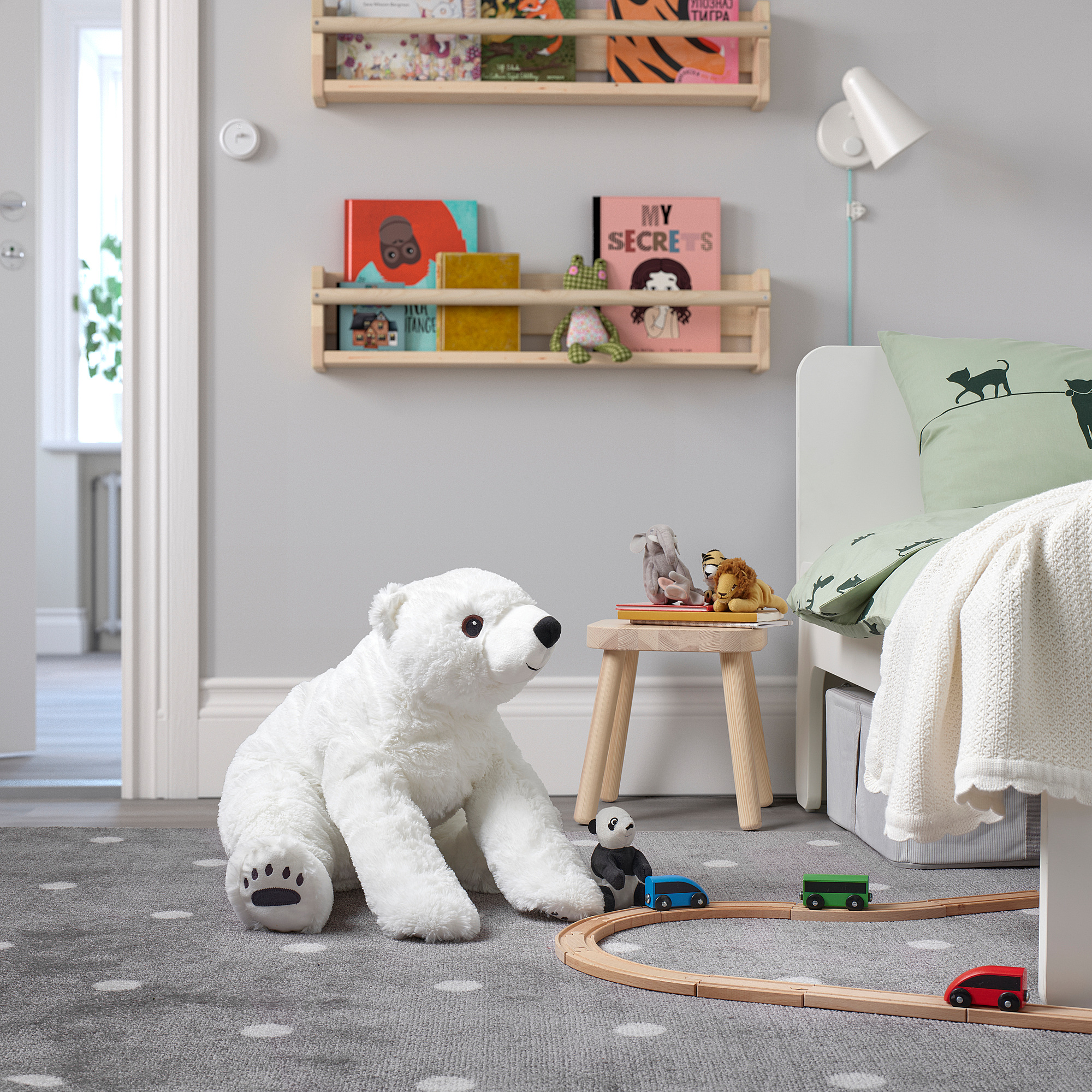 Large white stuffed polar bear sits beside bed, surrounded by toy train and books on shelves.