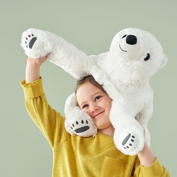 Happy girl holding up large plush polar bear toy on her arms, both smiling.