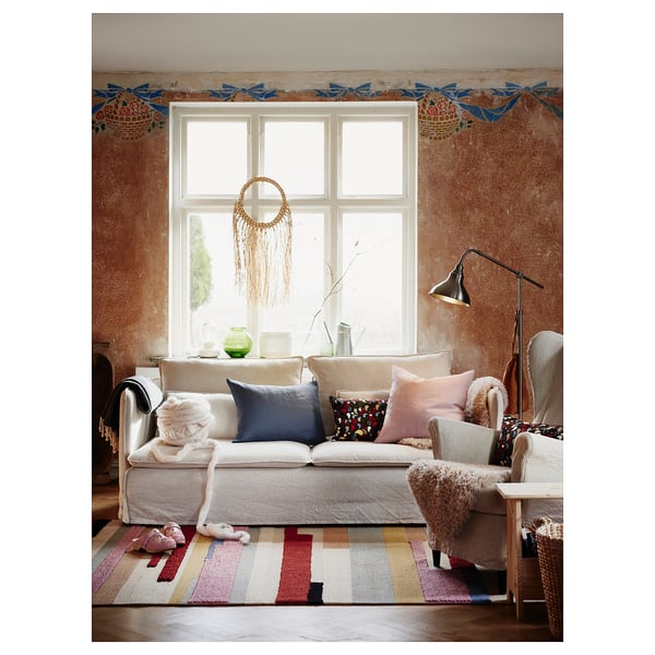 Cozy living room with SÖDERHAMN off-white sofa, colorful pillows, striped rug, and wall decor.