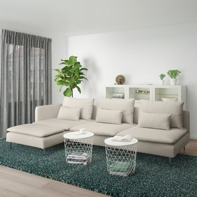 Modern living room: large beige sectional couch, green rug, white tables, plants, cabinets.