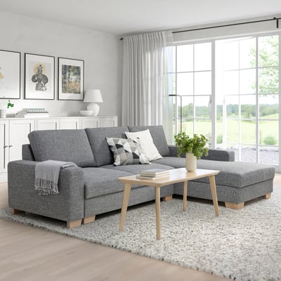 Modern grey l-shaped sofa with pillows, wooden coffee table, and large window in bright room.