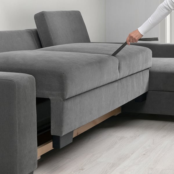 A hand pulls out a cushion from a grey modern sofa, revealing storage space.