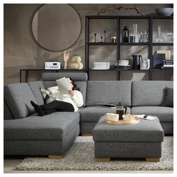 A modern living room with a gray SÖRVALLEN sofa, a person reading, and a coffee table with snacks.