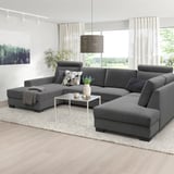 Modern gray l-shaped SÖRVALLEN sofa, large, with cushions, centered under pendant lamp, flanked by tall windows with curtains, on light rug.