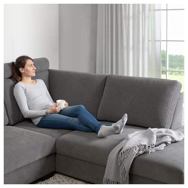 Woman relaxes on SÖRVALLEN sofa with mug, blanket nearby.