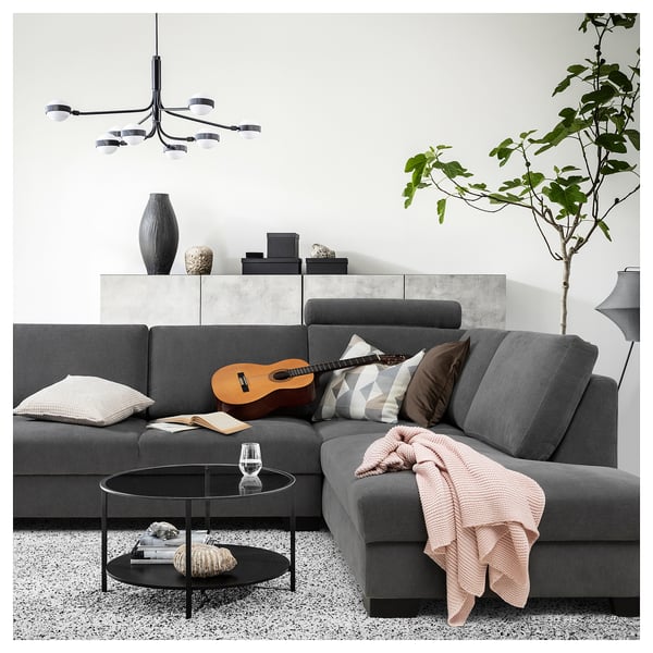 Modern gray sofa with cushions and blanket, round glass coffee table, guitar, and trendy lighting.