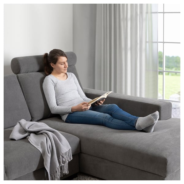 A woman reading on a gray SÖRVALLEN couch by a window.