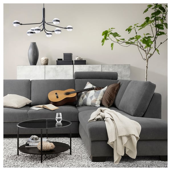Modern gray l-shaped sofa with pillows, blanket, guitar, books, glass, plant, and trendy decorations.