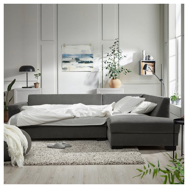 Modern grey sofa-bed with minimalist scandinavian design, white bedding, plant, lamp, and art.