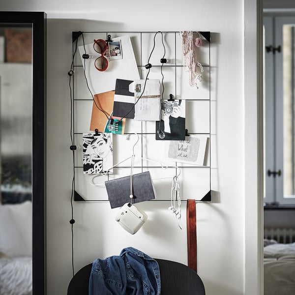 Modern memo board with black clips displays photos, notes on a white wall.