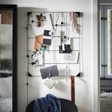 Modern memo board with black clips displays photos, notes on a white wall.
