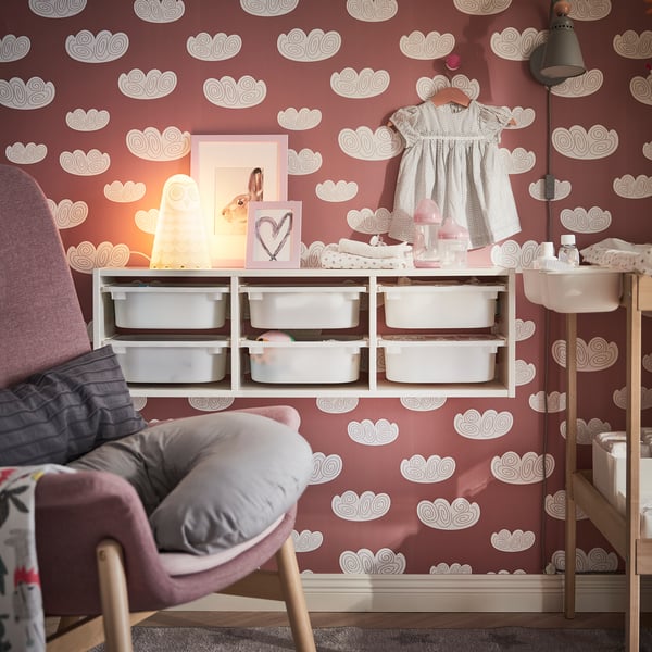 Cozy nursery with red cloud walls, soft lamp, gray armchair, white storage.