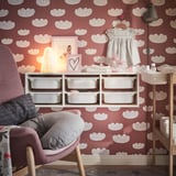 Cozy nursery with red cloud walls, soft lamp, gray armchair, white storage.