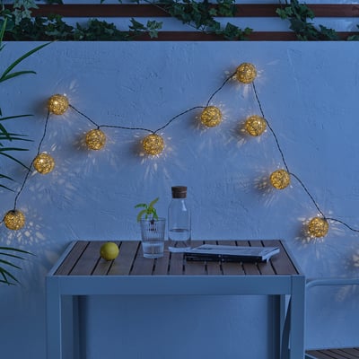 Gold lights warm a patio, illuminating a table with lemon, glass, carafe, and magazine.