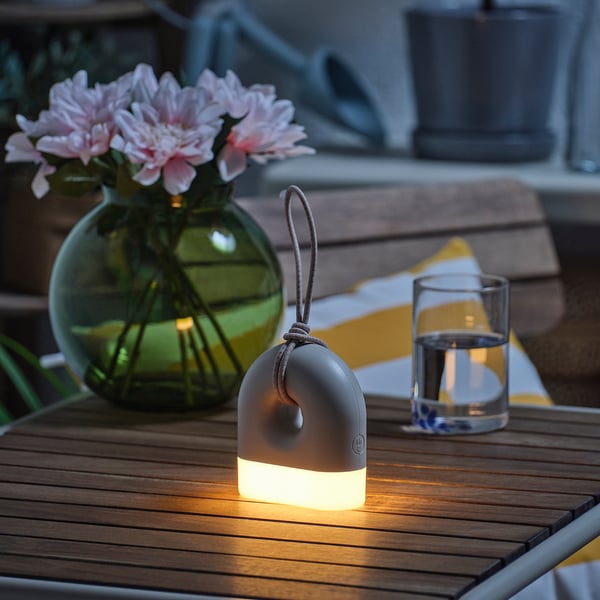 Lit outdoor lamp on wooden table beside glass vase with flowers and empty glass.