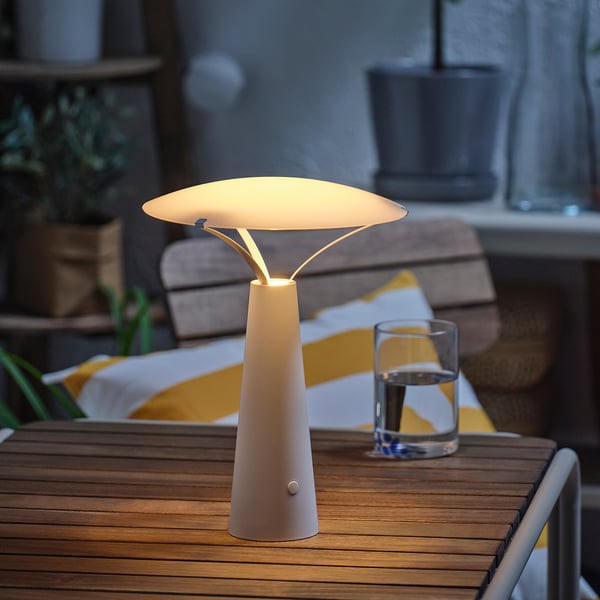 Modern table lamp on wooden table, providing warm decorative light, with glass of water nearby.