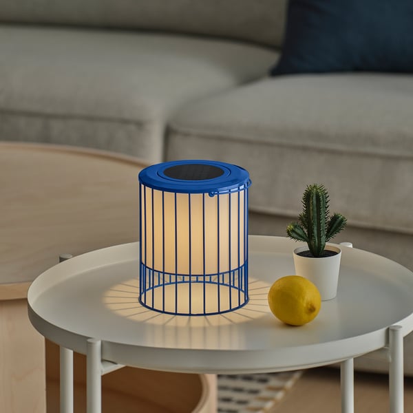 A blue SOLVINDEN solar-powered lamp on a white table, lit, with a lemon and cactus beside it.