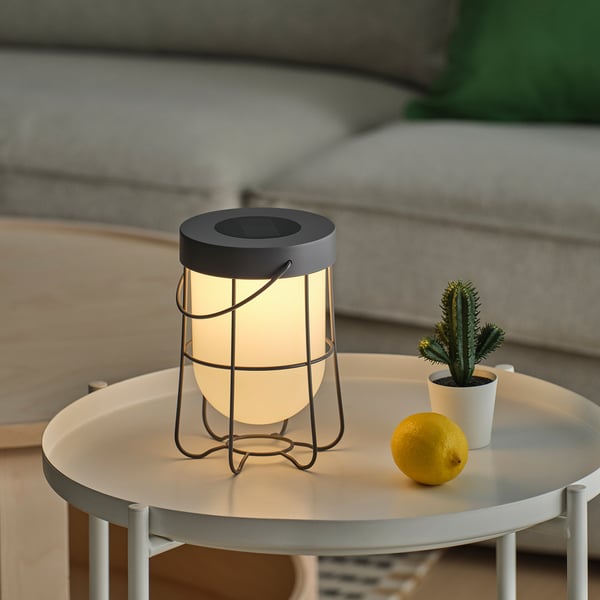 A solar-powered lantern on a table, illuminated, with a lemon and potted cactus nearby.