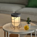 A solar-powered lantern on a table, illuminated, with a lemon and potted cactus nearby.