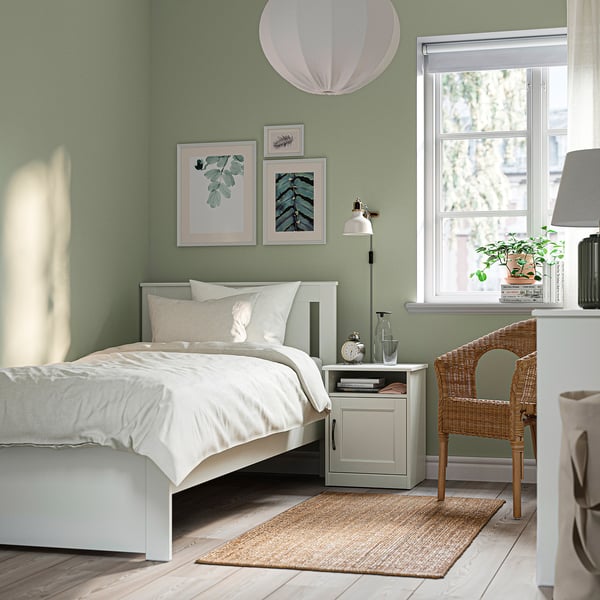 Cozy bedroom with SONGESAND bed, sage walls, crisp linens, rug, nightstand, lamp, plant, wicker chair, art, and large window.
