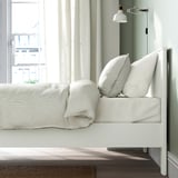 White bed frame with soft edges and high legs, designed for adjustable mattress thickness.