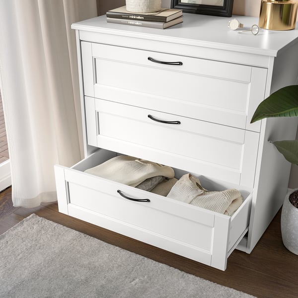 White dresser with open drawer, clothes, books, decor.