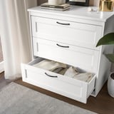 White dresser with open drawer, clothes, books, decor.