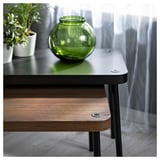 Minimalistic space-saving tables in dark wood and black metal, featuring a green vase and plant on top.
