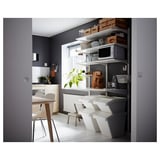 Modern kitchen with white furniture, including stackable SORTERA bins, a microwave, and dining table with chairs, against dark gray walls.