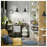 Well-organized kitchen corner with a yellow couch, blue rug, white wall clock, hanging lights, and a metal table with storage boxes in white and gray.