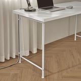 White desk with laptop, mouse, and lamp. Adjustable legs for uneven floors, cord management shown.
